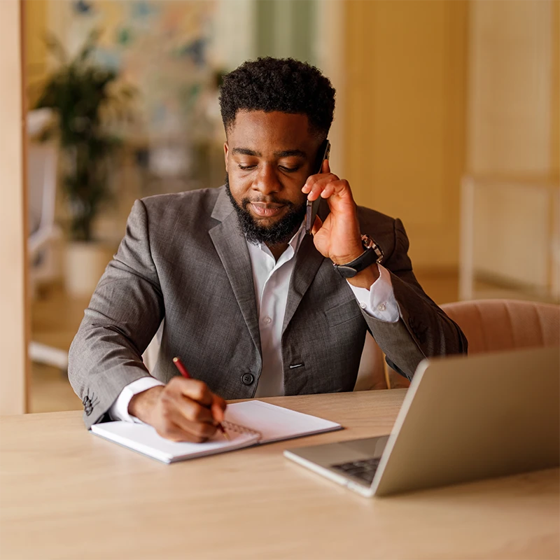 A man listens to his mobile phone while taking notes on a pad.